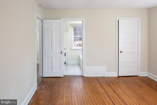 unfurnished bedroom with wood-type flooring, connected bathroom, and baseboards