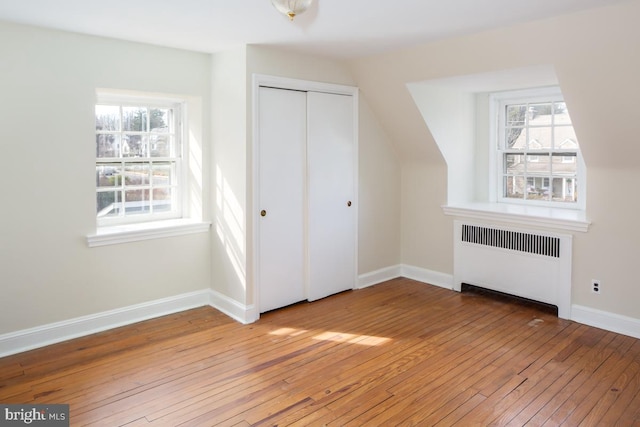 unfurnished bedroom with a closet, baseboards, light wood finished floors, and radiator heating unit