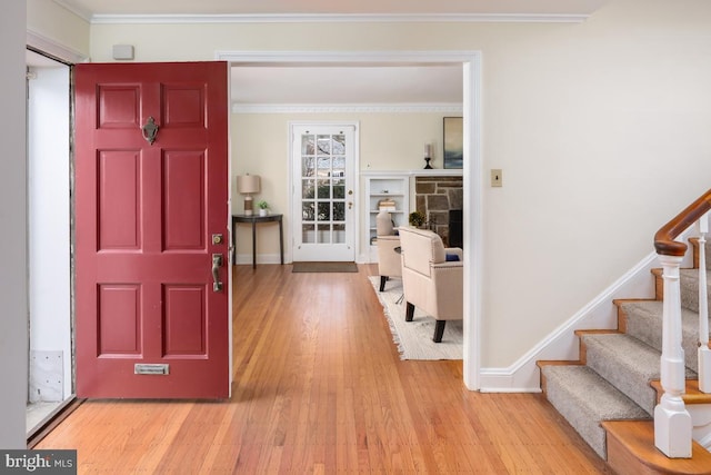 entryway with a fireplace, baseboards, stairs, light wood finished floors, and crown molding