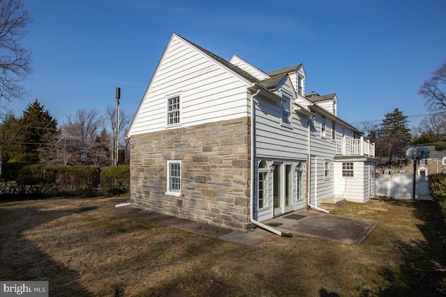 view of side of home featuring stone siding, a patio area, a yard, and fence