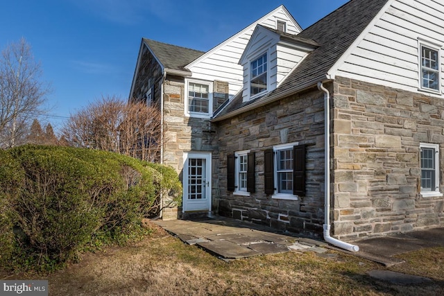 view of property exterior featuring stone siding and a shingled roof