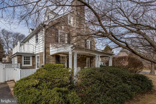 view of property exterior featuring stone siding, fence, a chimney, and a balcony