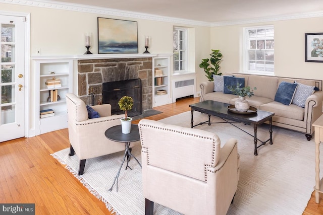 living area with a stone fireplace, ornamental molding, radiator heating unit, and wood-type flooring