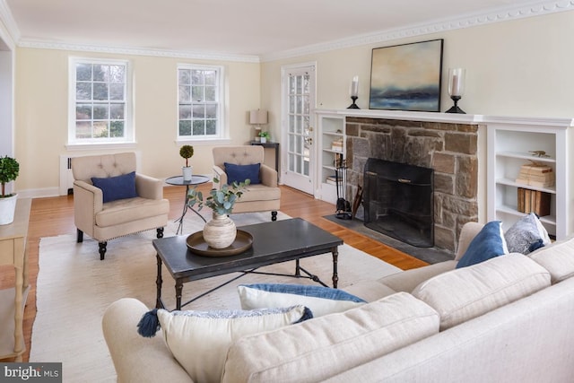 living room with ornamental molding, a stone fireplace, wood finished floors, and baseboards