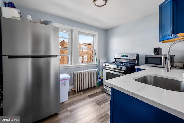 kitchen with light hardwood / wood-style flooring, sink, blue cabinetry, stainless steel appliances, and radiator