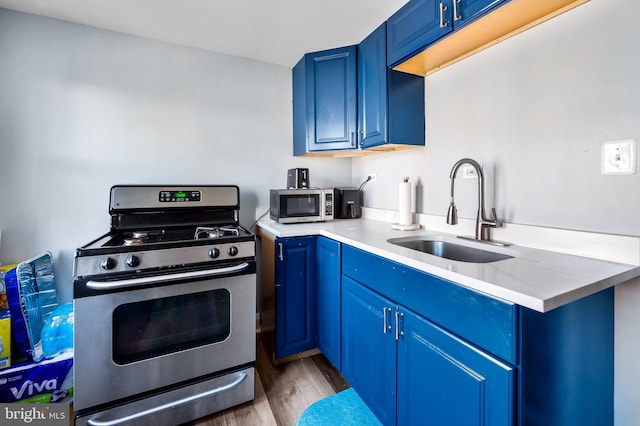 kitchen with blue cabinetry, appliances with stainless steel finishes, sink, and light hardwood / wood-style flooring