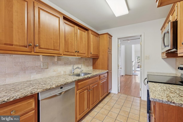 kitchen featuring light tile patterned floors, backsplash, appliances with stainless steel finishes, brown cabinetry, and a sink