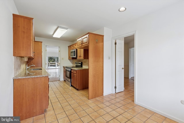 kitchen featuring light tile patterned floors, light stone counters, stainless steel appliances, a sink, and tasteful backsplash