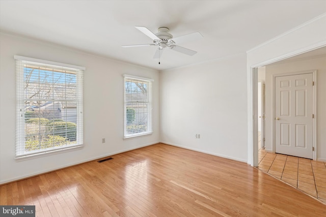 empty room featuring crown molding, light wood finished floors, visible vents, and a healthy amount of sunlight