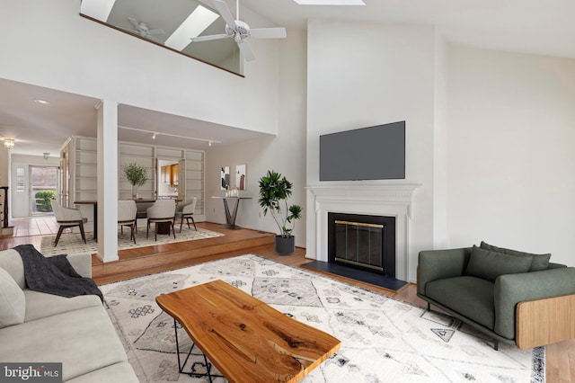 living area featuring a ceiling fan, a glass covered fireplace, a high ceiling, and wood finished floors