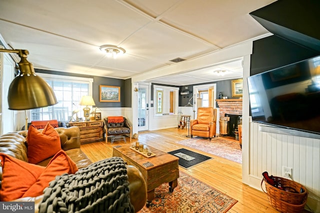 living room featuring a wainscoted wall, a brick fireplace, wood finished floors, and visible vents