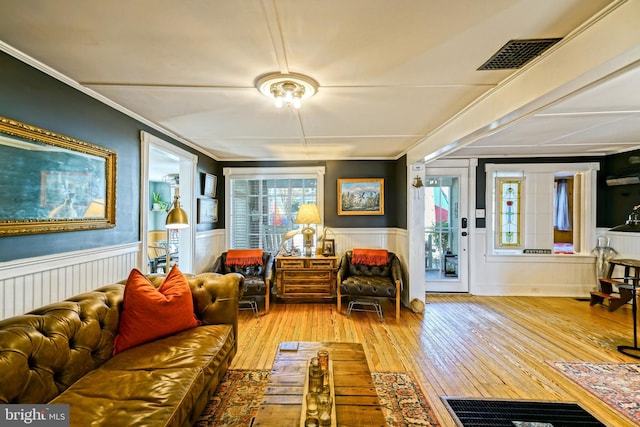 living area with ornamental molding, wainscoting, visible vents, and light wood-style flooring