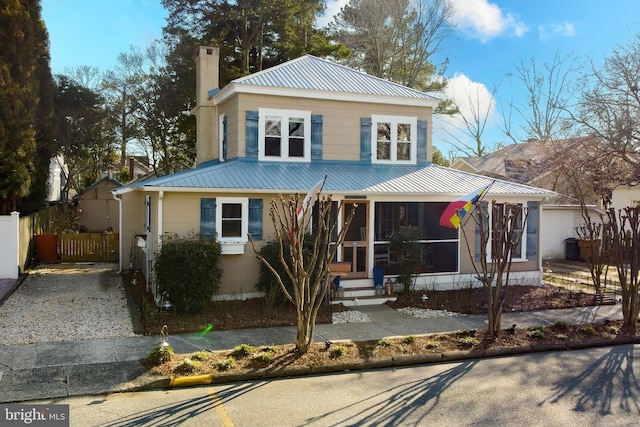 view of front of property with a sunroom, metal roof, a chimney, and fence