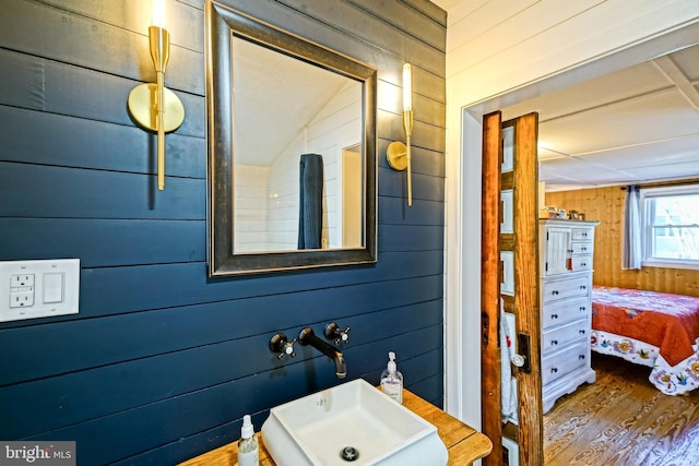 ensuite bathroom featuring wood finished floors, ensuite bath, a sink, and wood walls