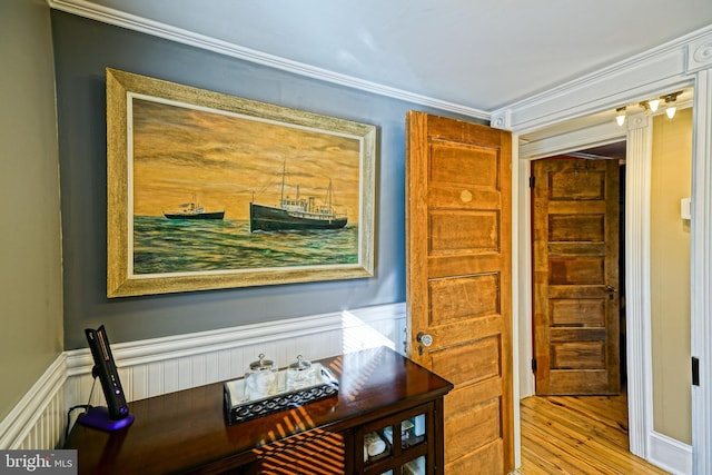 hallway with a wainscoted wall, crown molding, and light wood-style flooring