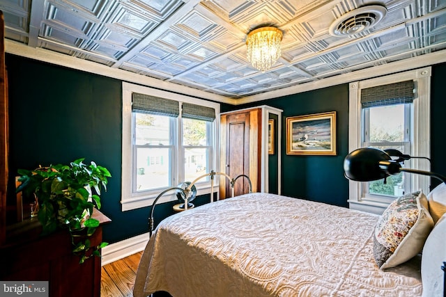 bedroom featuring wood finished floors, visible vents, baseboards, an ornate ceiling, and an inviting chandelier