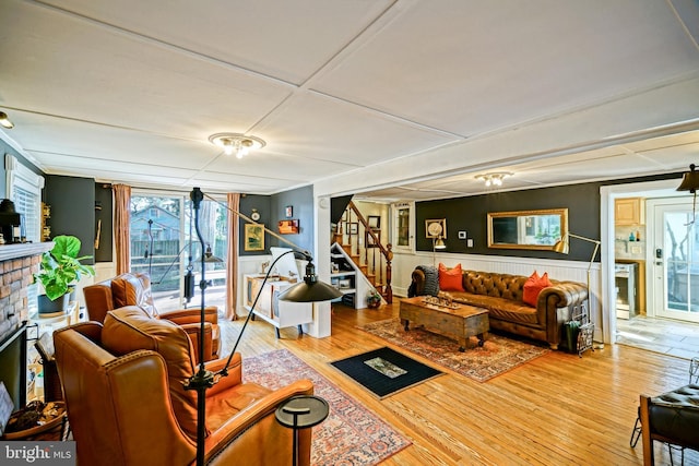 living room featuring a brick fireplace, wainscoting, stairway, and wood finished floors