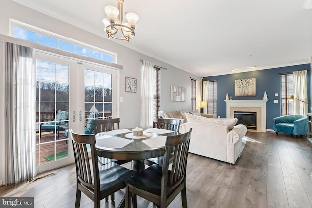 dining room with french doors, wood-type flooring, visible vents, ornamental molding, and a glass covered fireplace