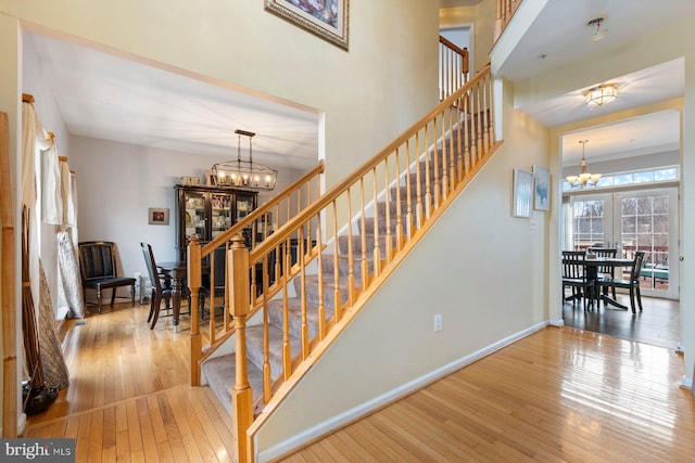 staircase featuring wood-type flooring, a notable chandelier, baseboards, and french doors