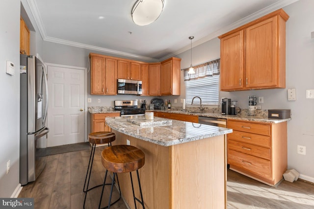 kitchen with appliances with stainless steel finishes, ornamental molding, a sink, a kitchen island, and wood finished floors