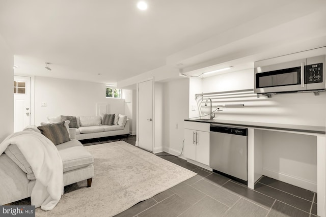 kitchen with light countertops, appliances with stainless steel finishes, white cabinets, a sink, and baseboards