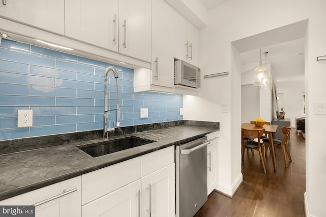 kitchen with hanging light fixtures, stainless steel dishwasher, white microwave, white cabinetry, and a sink