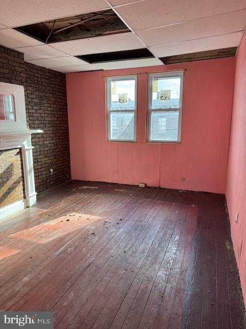 unfurnished living room with a paneled ceiling, dark wood-style floors, brick wall, and a fireplace