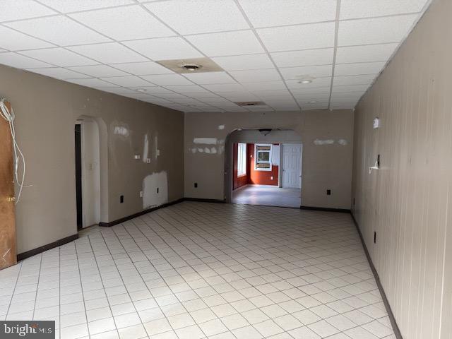 spare room with arched walkways, a paneled ceiling, and baseboards