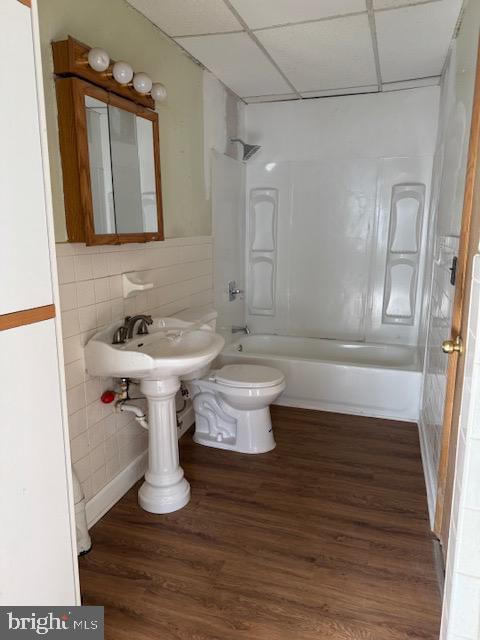 bathroom featuring shower / bath combination, toilet, wood finished floors, a paneled ceiling, and tile walls