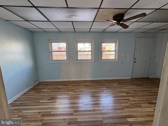 unfurnished room with a ceiling fan, baseboards, a drop ceiling, and wood finished floors