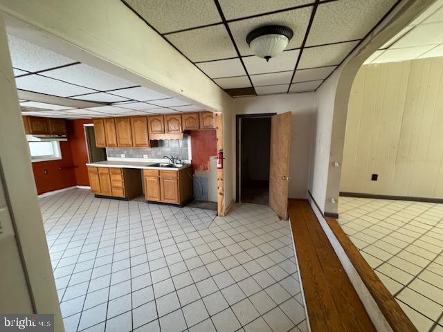 kitchen with arched walkways, light countertops, brown cabinetry, a sink, and a drop ceiling