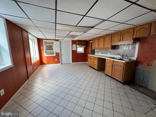 kitchen featuring tasteful backsplash, a paneled ceiling, light countertops, brown cabinetry, and a sink