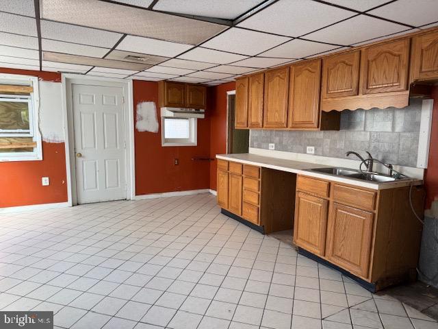 kitchen featuring wall oven, a sink, light countertops, brown cabinets, and tasteful backsplash