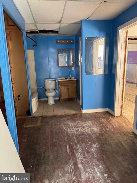 bathroom featuring a paneled ceiling, toilet, vanity, wood finished floors, and baseboards