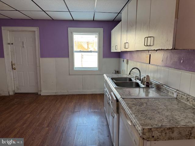 kitchen with a wainscoted wall, wood finished floors, light countertops, a paneled ceiling, and a sink