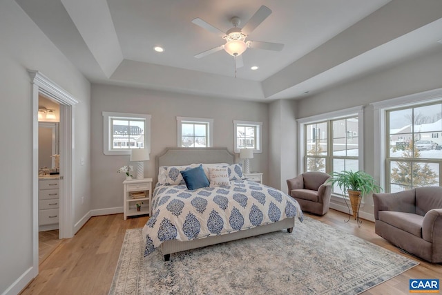 bedroom with a tray ceiling, ceiling fan, connected bathroom, and light hardwood / wood-style floors