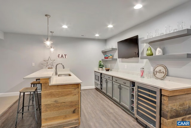 kitchen featuring stainless steel microwave, pendant lighting, sink, light wood-type flooring, and wine cooler