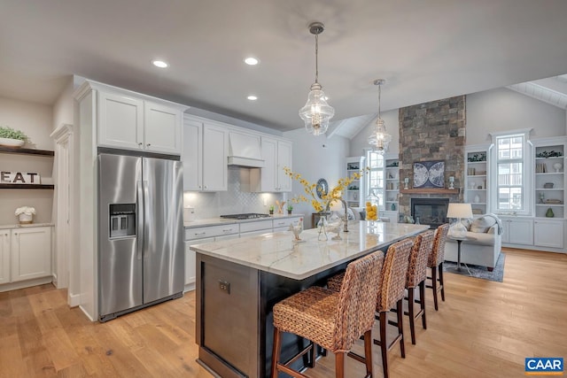 kitchen featuring appliances with stainless steel finishes, a center island with sink, a breakfast bar area, light stone countertops, and white cabinets