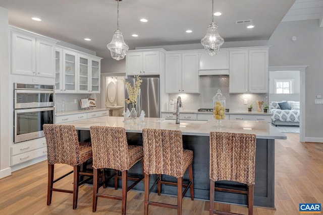 kitchen with decorative light fixtures, stainless steel appliances, white cabinetry, and a large island with sink