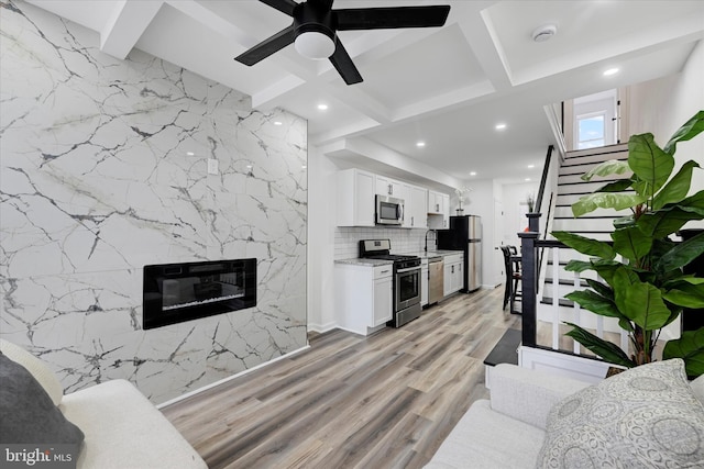 kitchen with appliances with stainless steel finishes, white cabinetry, light hardwood / wood-style floors, beam ceiling, and tasteful backsplash