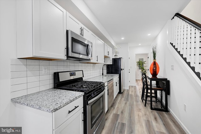 kitchen with appliances with stainless steel finishes, light hardwood / wood-style flooring, light stone counters, white cabinetry, and tasteful backsplash