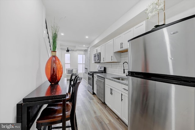 kitchen with sink, appliances with stainless steel finishes, white cabinetry, and light stone countertops