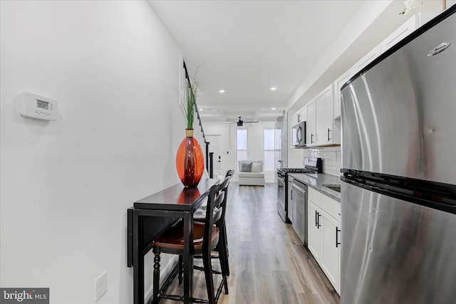 kitchen with white cabinets, dark stone countertops, stainless steel appliances, and backsplash