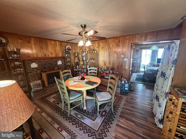 dining space featuring dark wood finished floors, ceiling fan, a textured ceiling, wood walls, and a fireplace