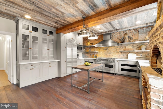 kitchen with glass insert cabinets, light countertops, wall chimney range hood, and built in appliances