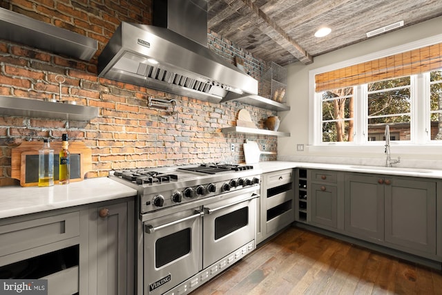 kitchen featuring gray cabinets, light countertops, a sink, double oven range, and wall chimney exhaust hood