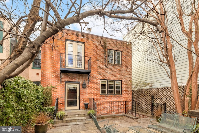 view of front facade with brick siding, a patio area, fence, and a balcony