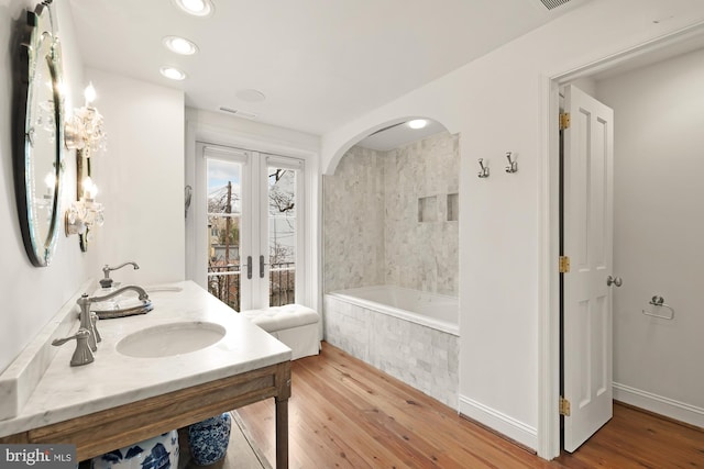 full bathroom featuring double vanity, wood finished floors, a garden tub, french doors, and a sink