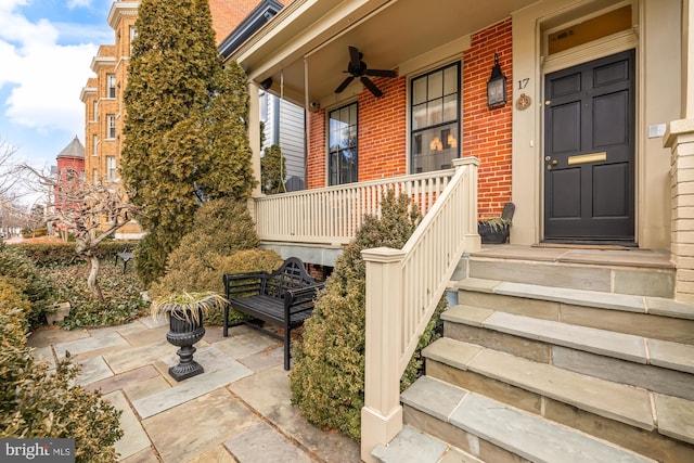 entrance to property with ceiling fan, a porch, and brick siding