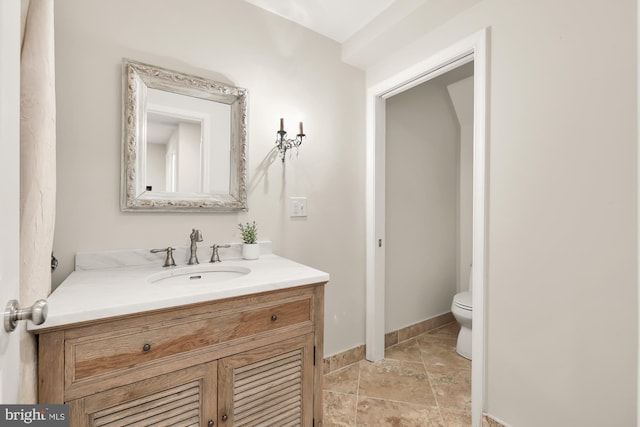 bathroom featuring stone finish floor, baseboards, vanity, and toilet